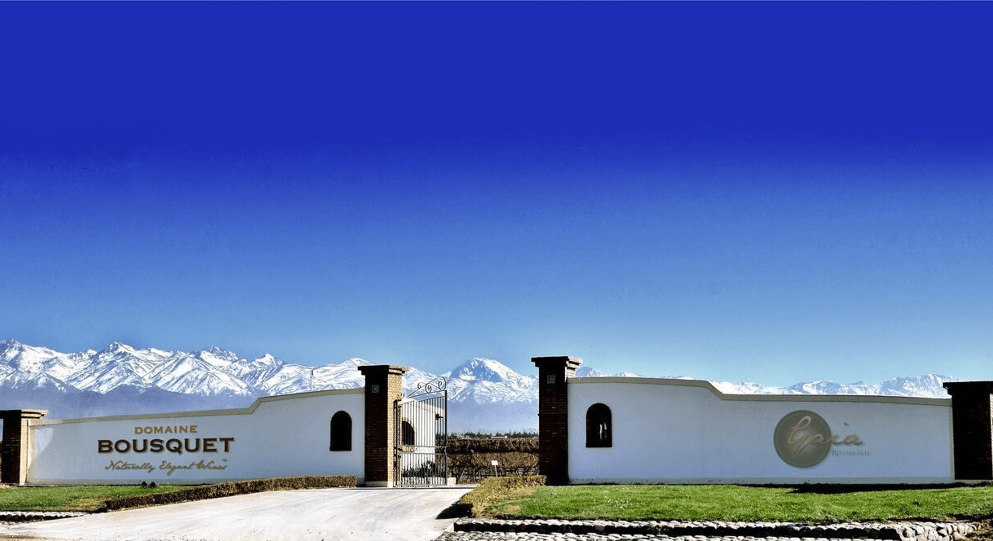 Landscape image of the front gates of Domaine Bousquet, with mountains and a blue sky.